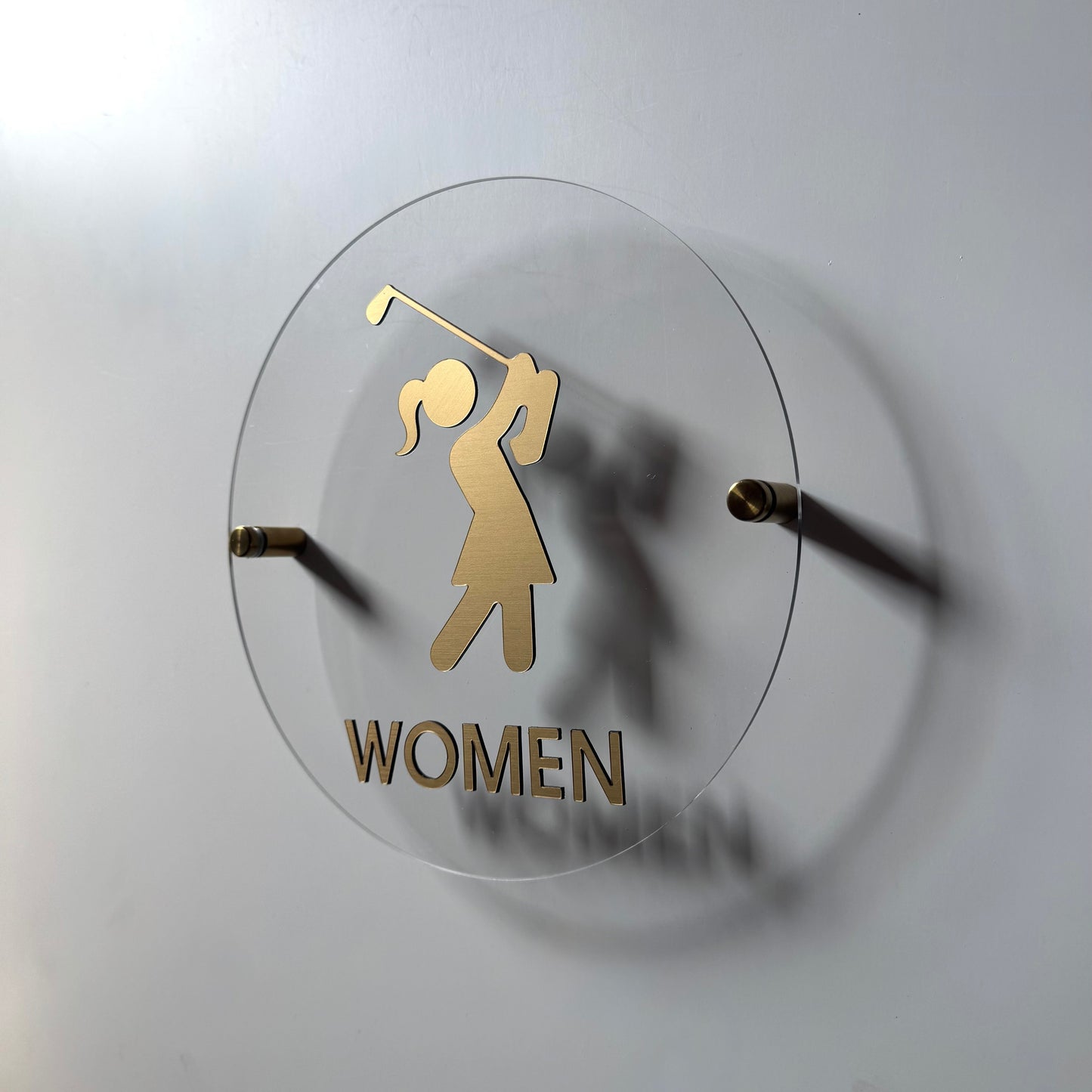 Golf-themed wall sign with a gold silhouette of a golfer and 'WOMEN' text on a white background.