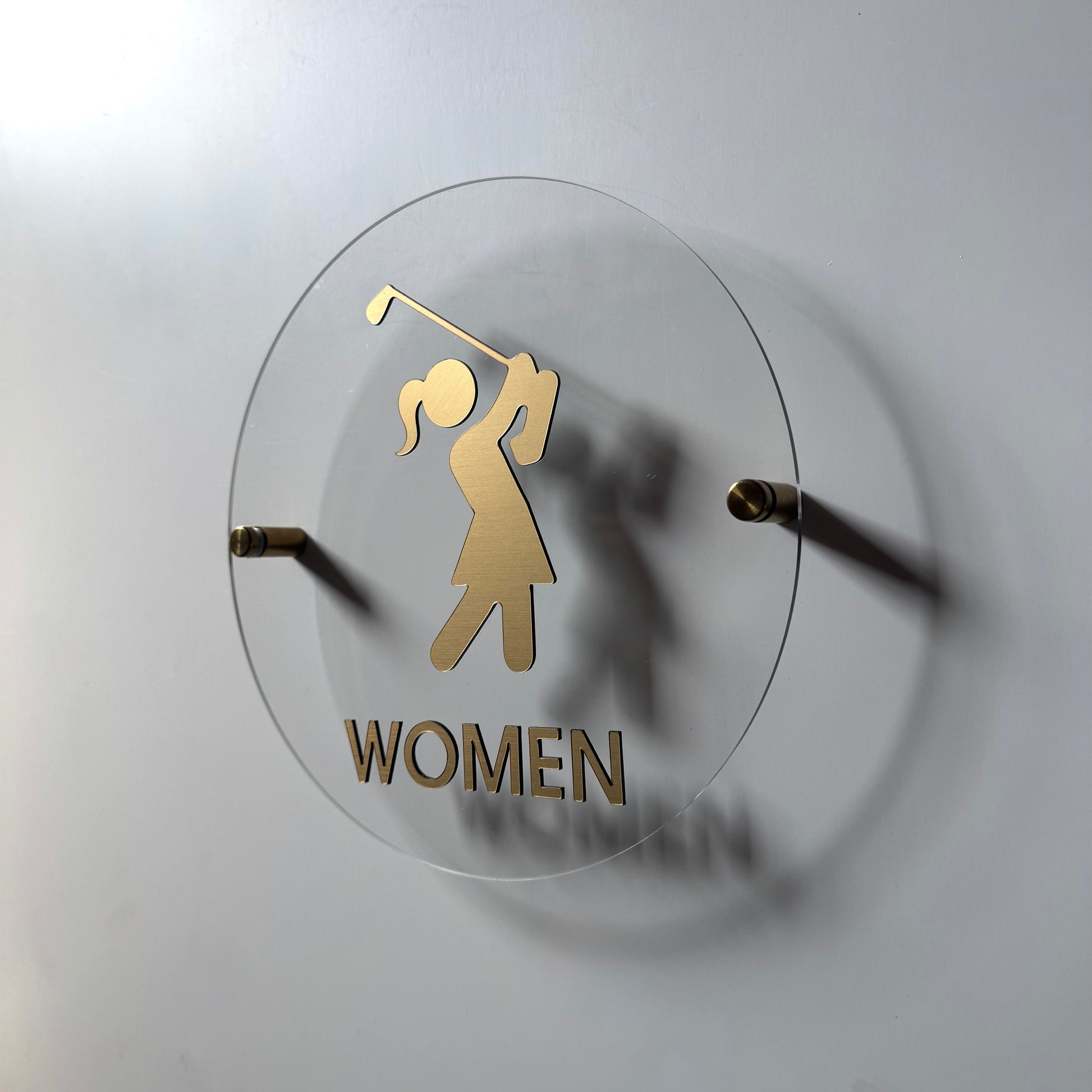 Golf-themed wall sign with a gold silhouette of a golfer and 'WOMEN' text on a white background.